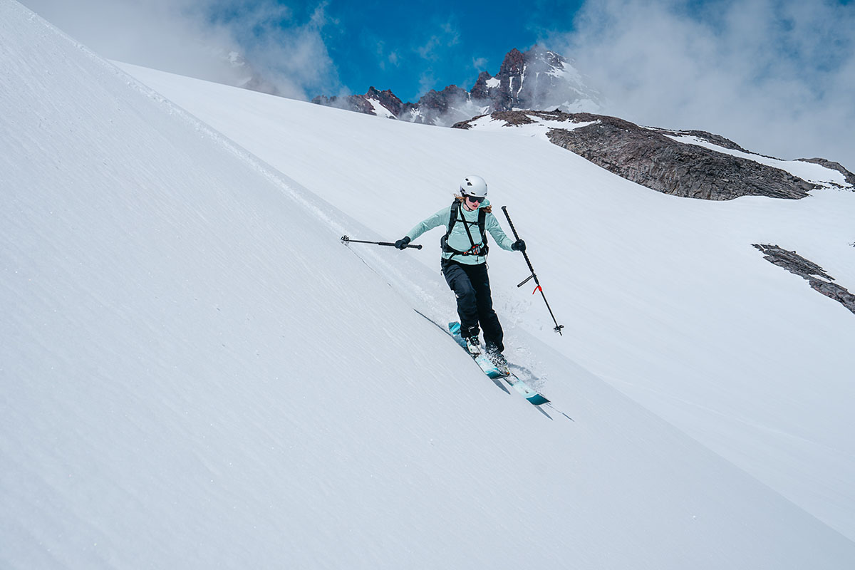 A woman skiing down a steep snowy slope with ski poles