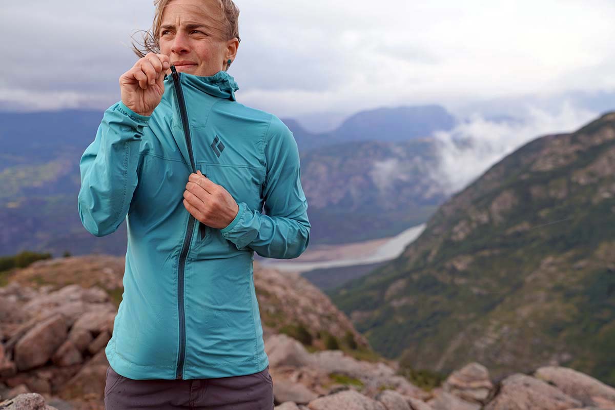 a woman zipping up a blue jacket on a ridgeline