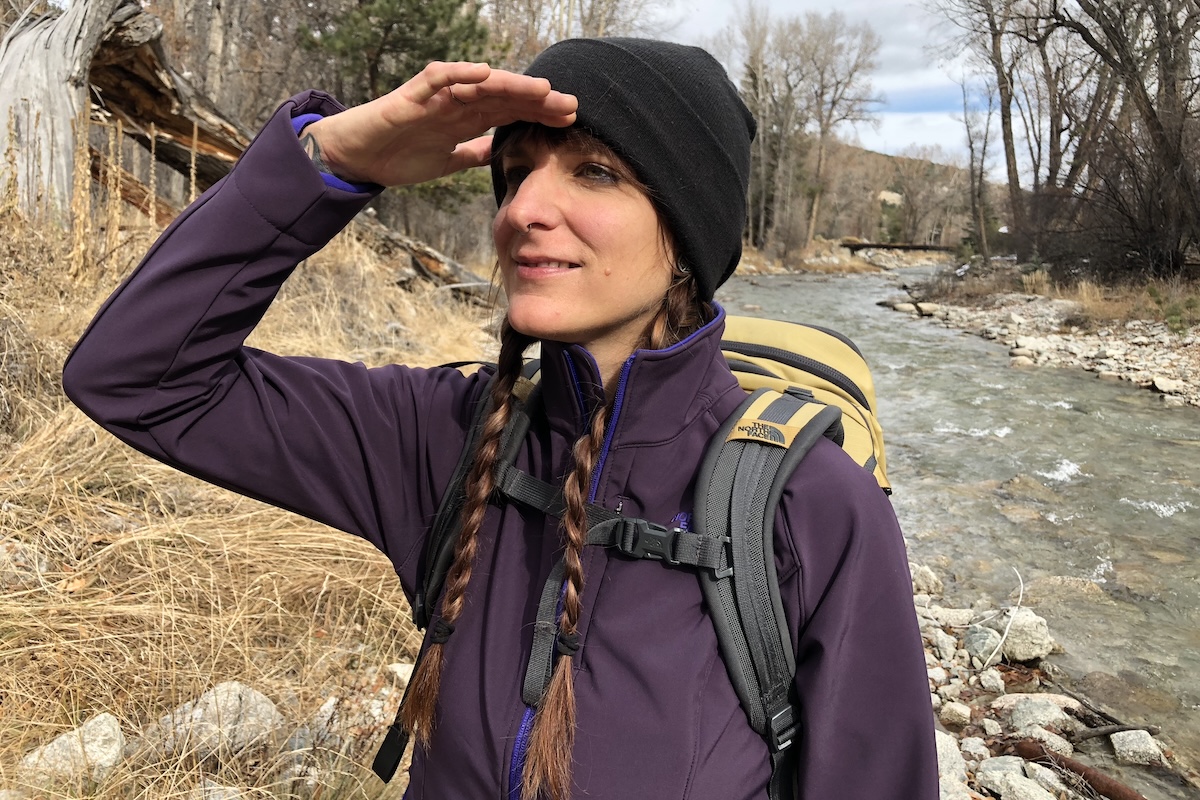 A woman in a purple jacket puts here hands up over her eyes to look off in the distance