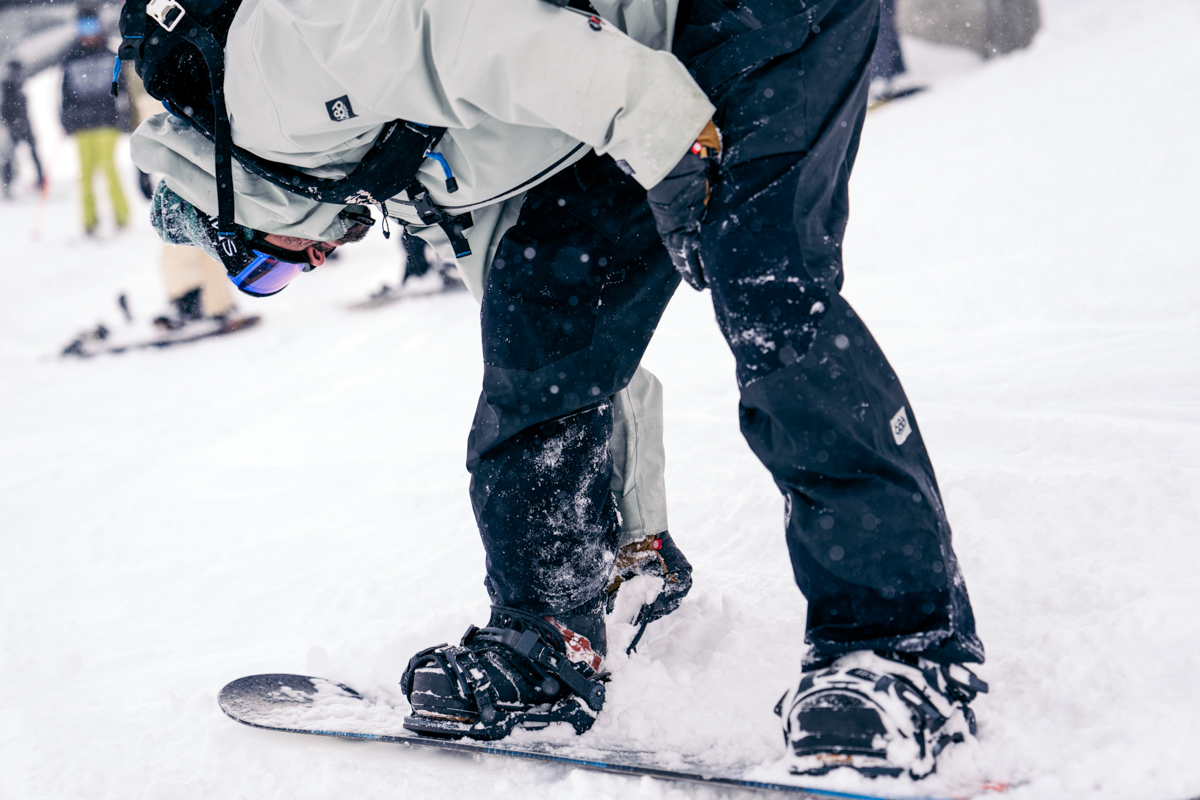A snowboarder strapping into bindings at the top of the run