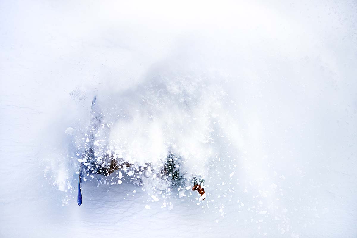 A snowboarder wipes out on a mountain, and is covered in snow from top to bottom.