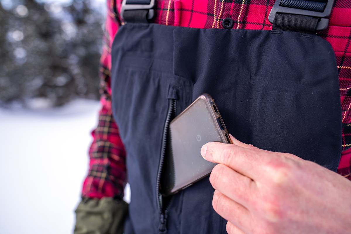 A person putting their phone into the chest pocket on some bibs