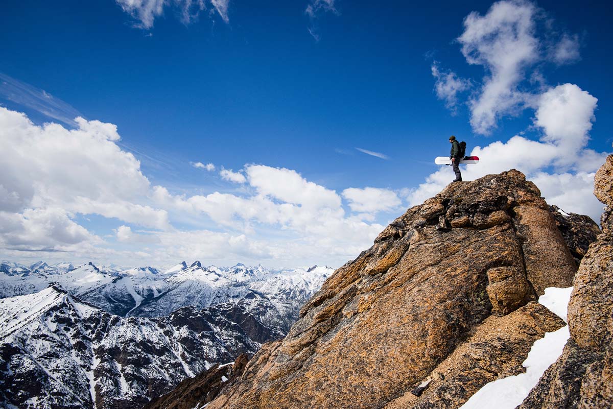 A snowboarder standing on top of a rocky peak