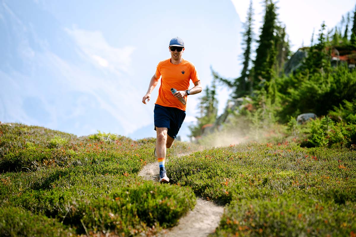 A man in an orange shirt is trail running in the Brooks Cascadia shoe
