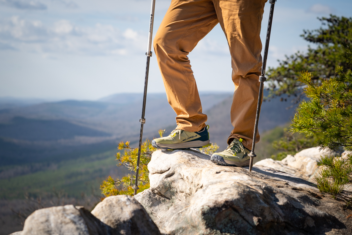 A hiker stands on a rocky outcropping, wearing Lone Peak trail runners.