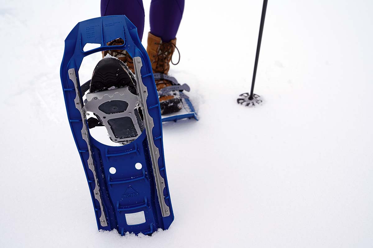 A close up of the crampons on the bottom of a blue snowshoe