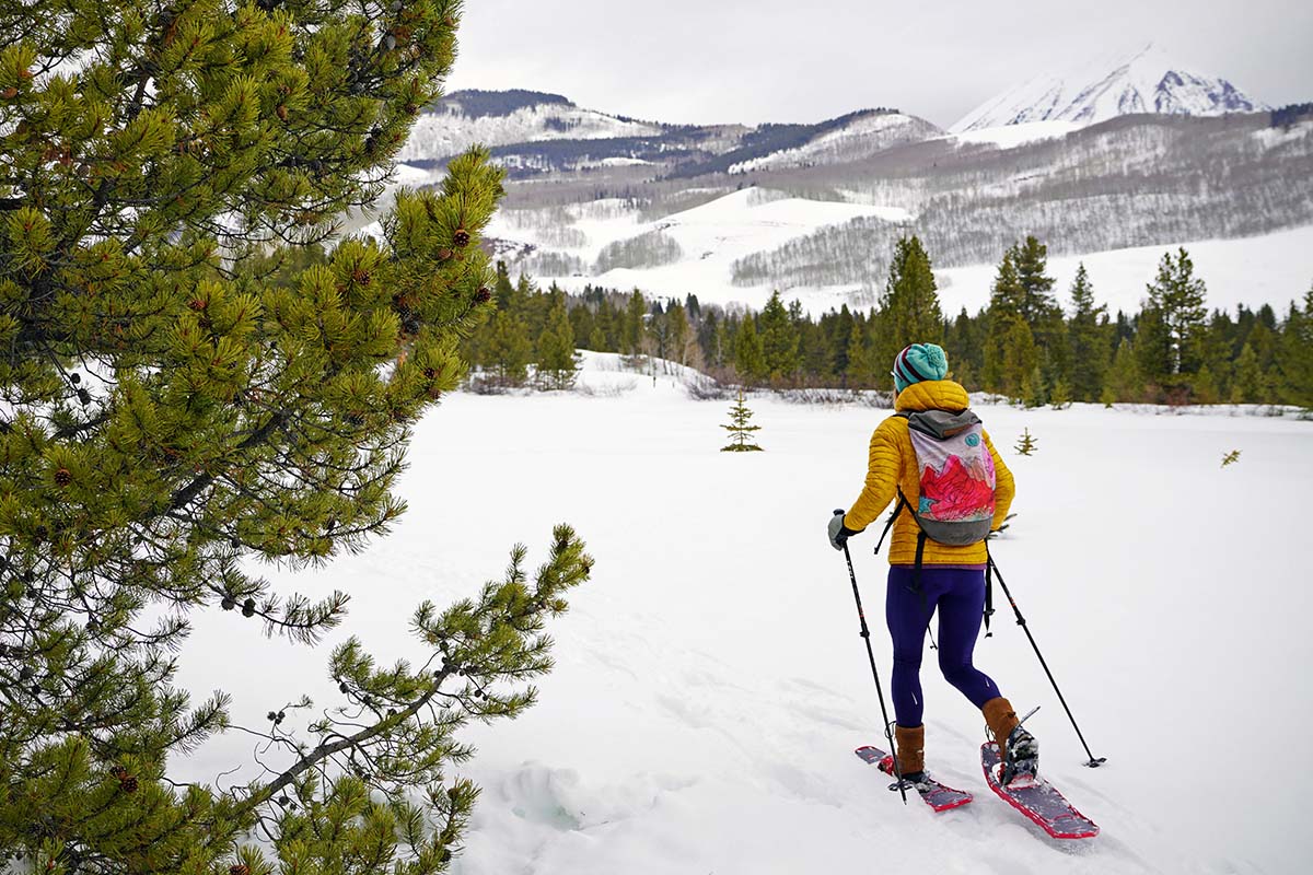 A woman hiking through a forest wearing snowshoes