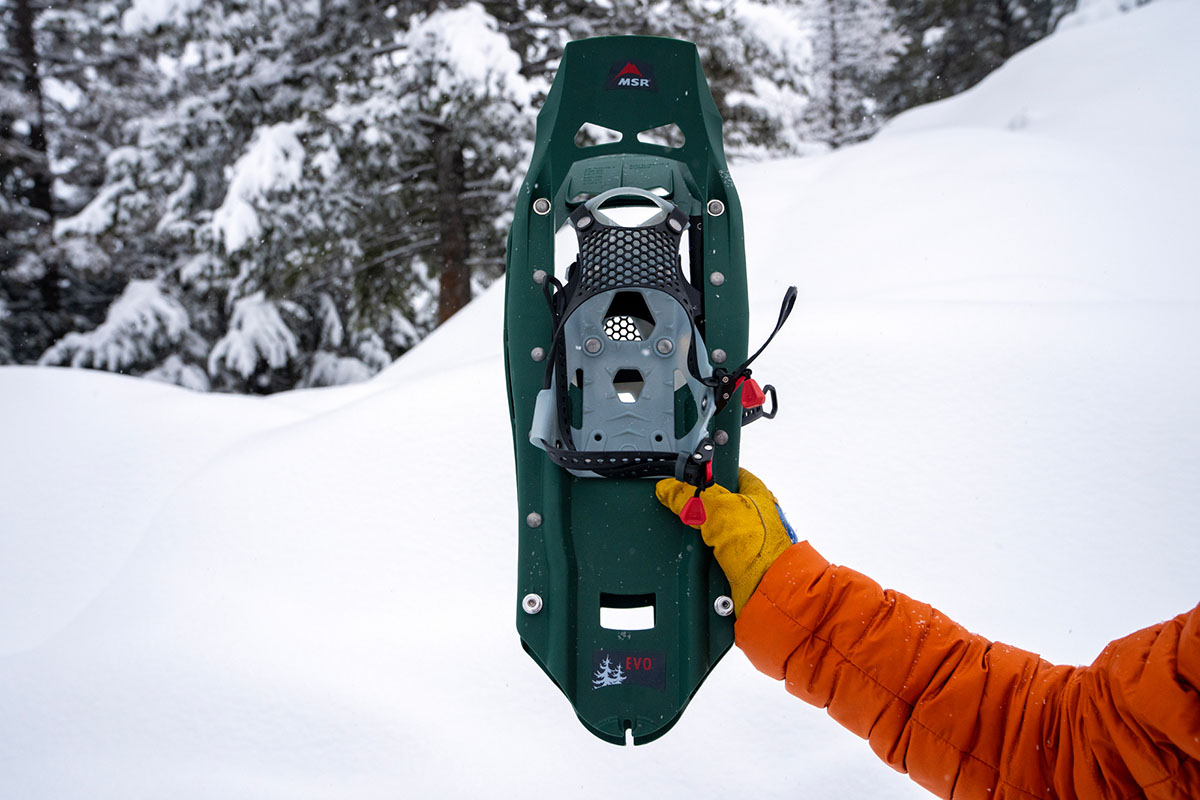 Holding up a green snowshoe in a snowy forest