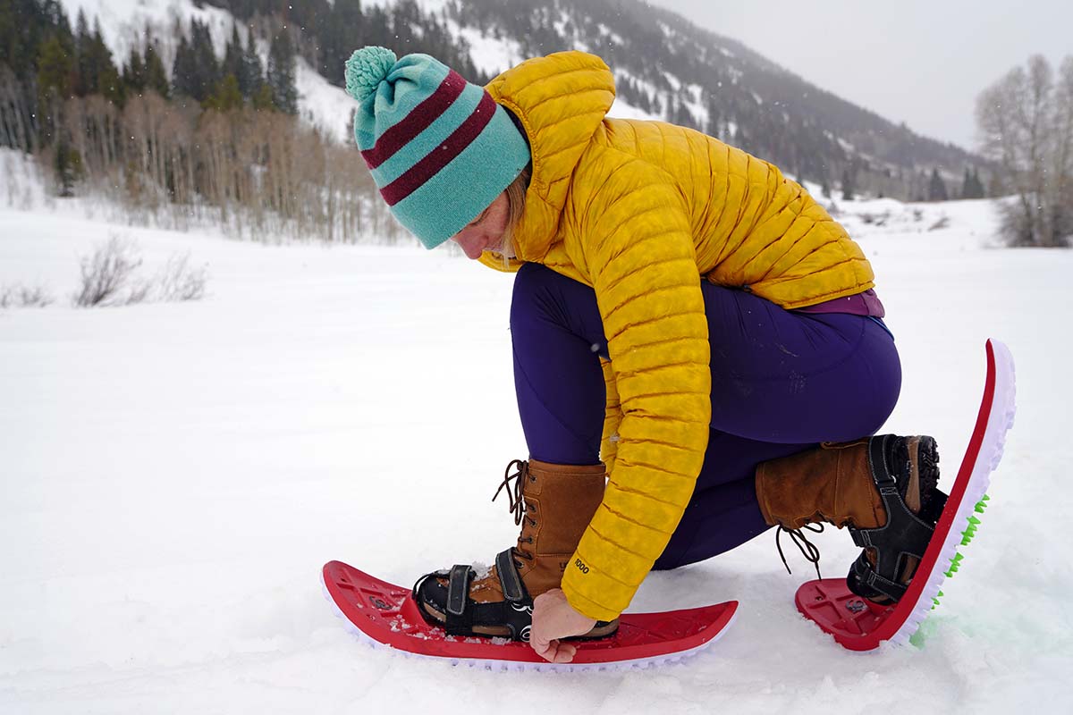 A woman adjusting the bindings on a red snowshoe