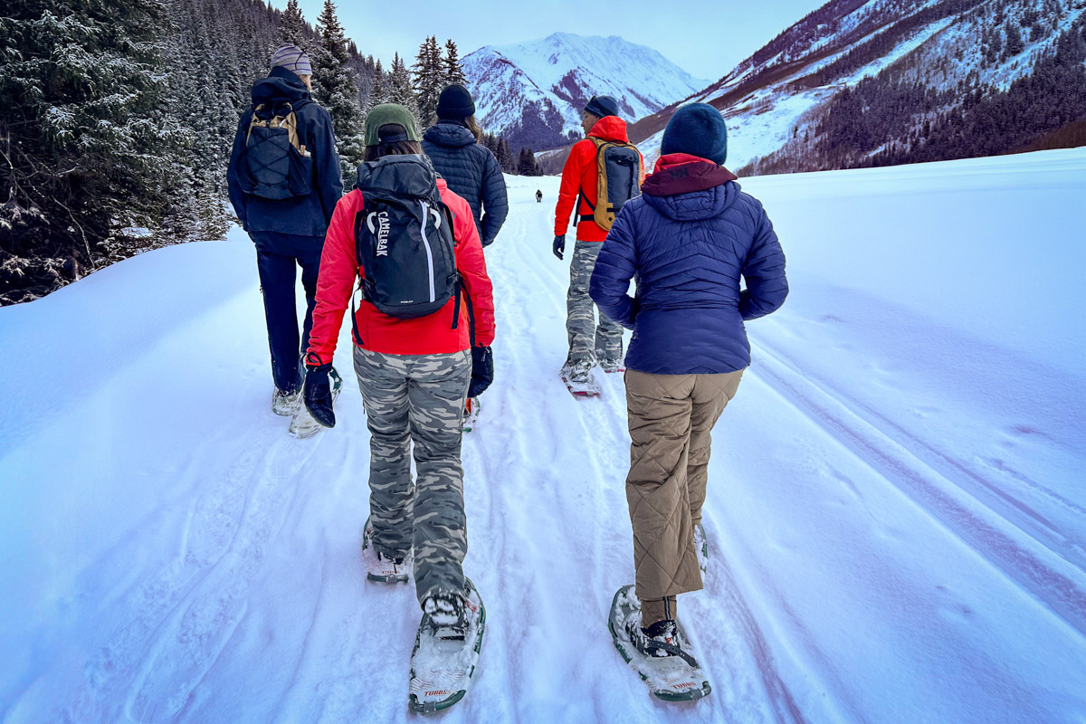 Several people snowshowing on a snowy trail