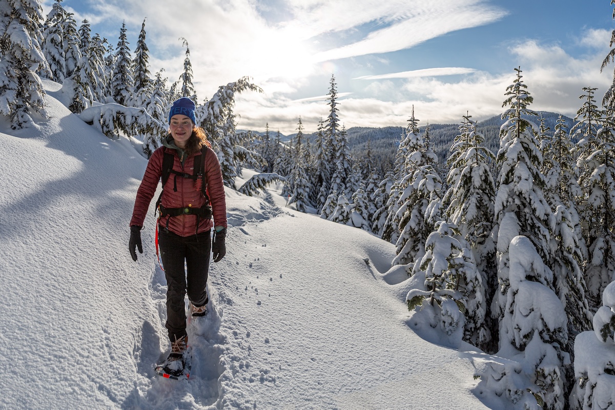 A woman walks through a snowy forest with snowshoes