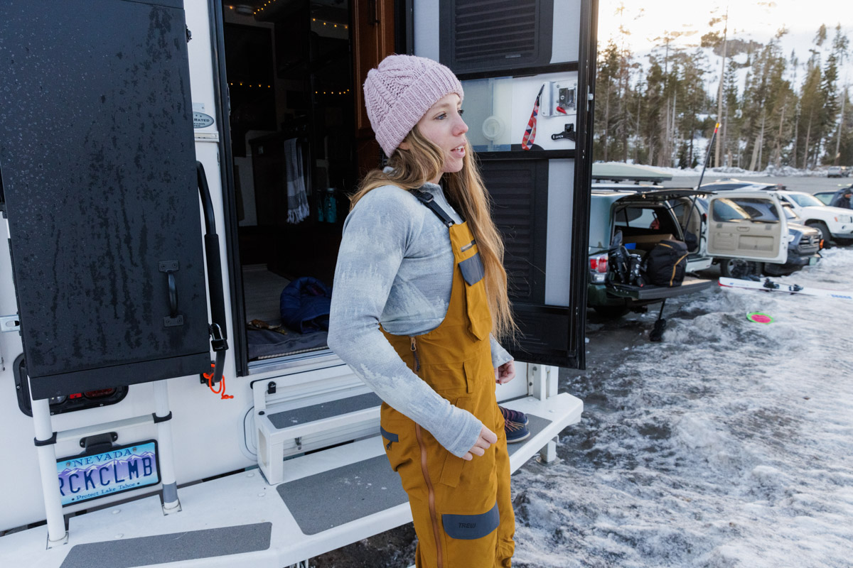 A woman wearing a white baselayer and ski bibs