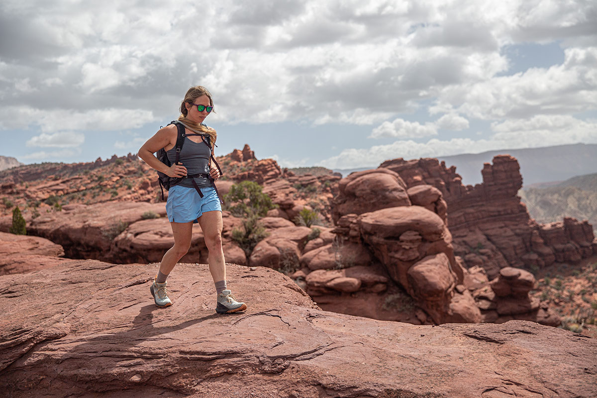 A hiker walks on top of bright red rocks in the Utah desert.