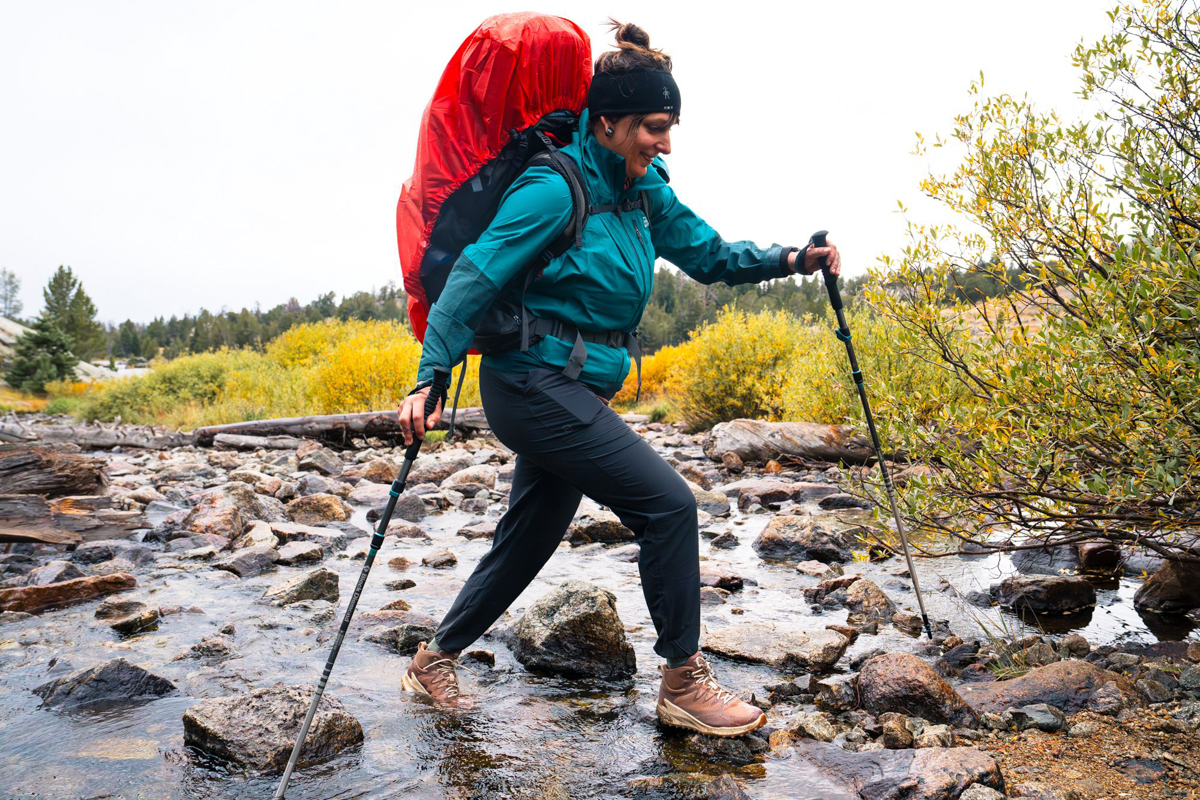 A backpacker crosses a stepping stone bridge over a stream.