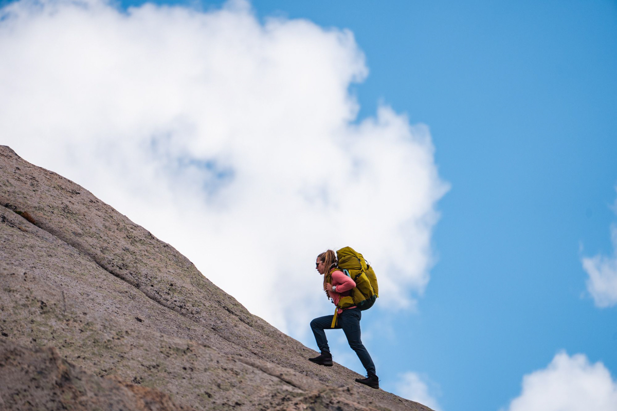 A woman treks up a steep rock. 