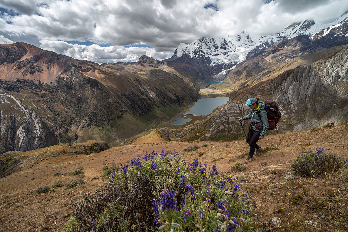 A hiker is seen over a stunning mountain overlook dotted with clouds and spring flowers.