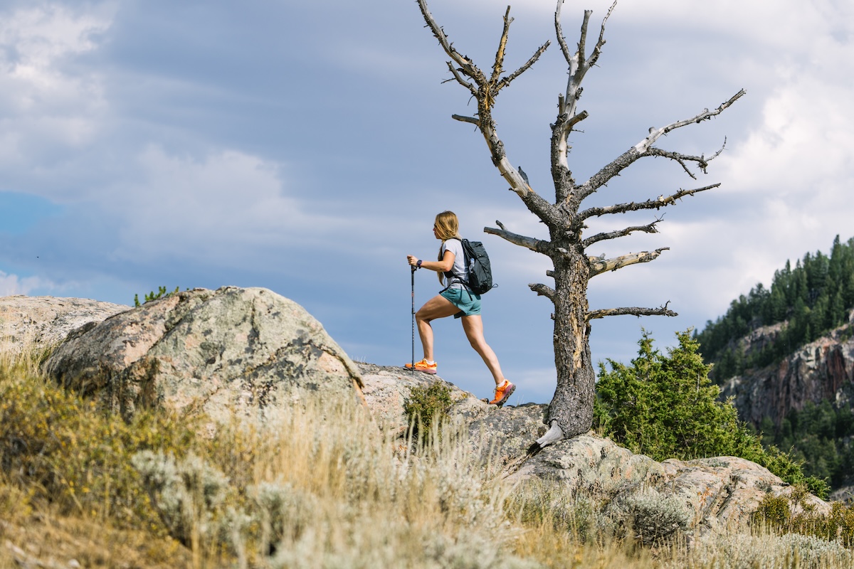 a woman is hiking up a peak wearing orange trail running shoes