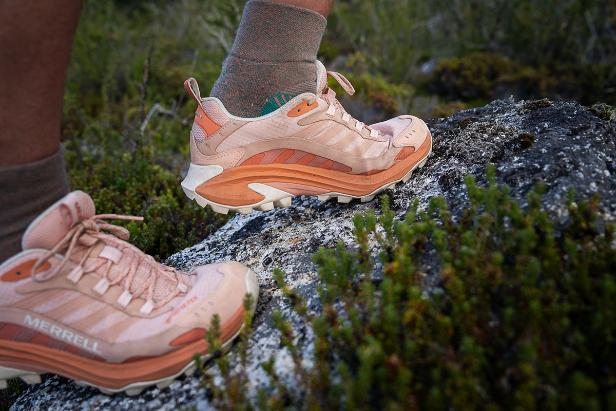 The side view of Merrell Speed 2 shoes are shown as a woman walks up a rock in a close up