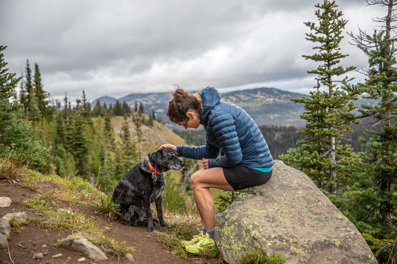 a woman sits on a rock overlooking a green valley