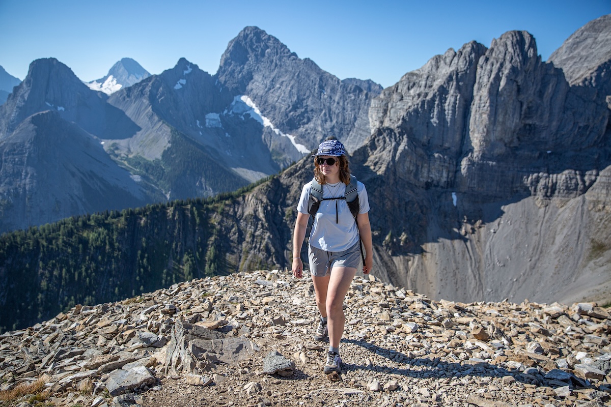 A woman walks over talus with the mountains behind her 