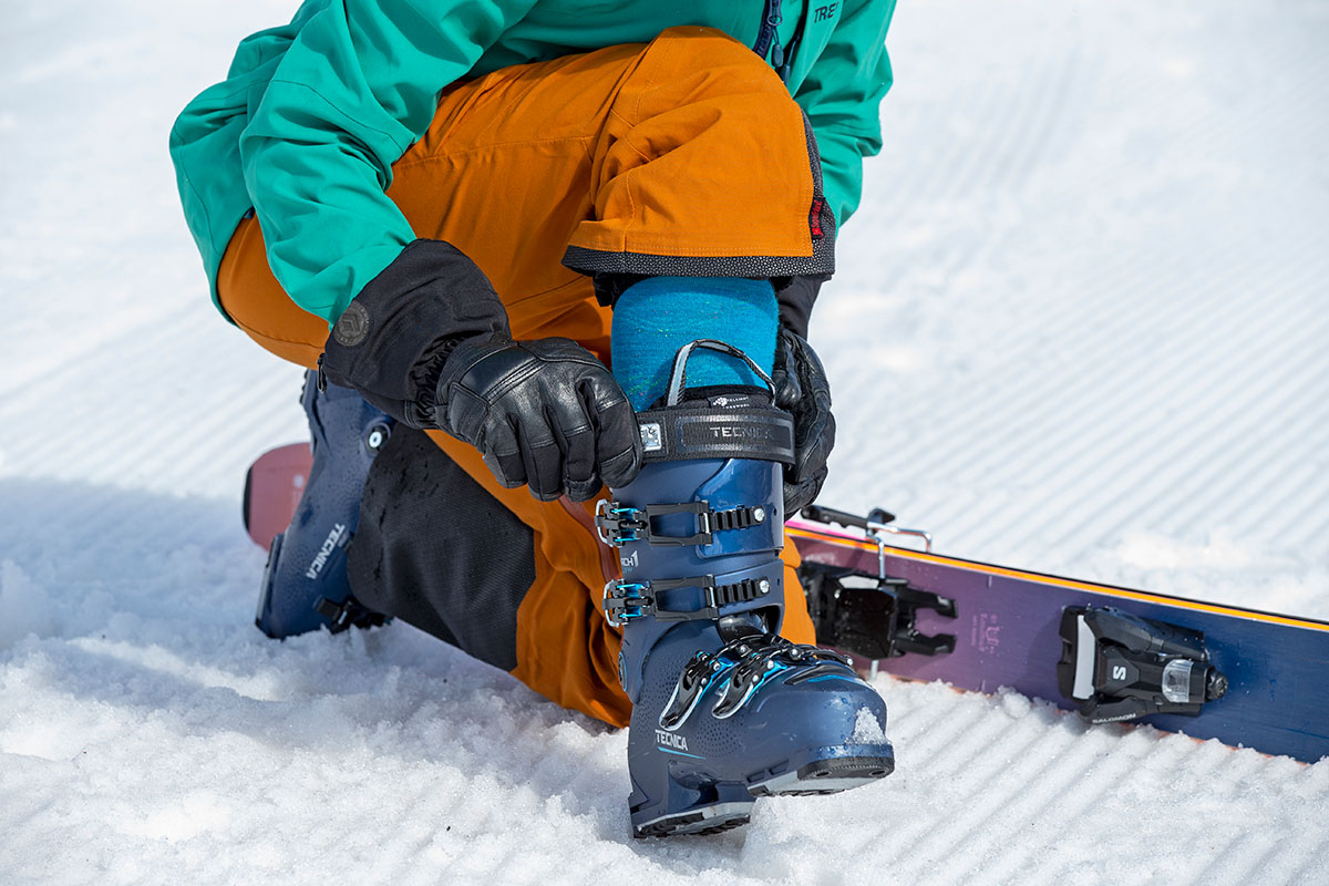 A skier kneels down to adjust the Technica Mach1 LV