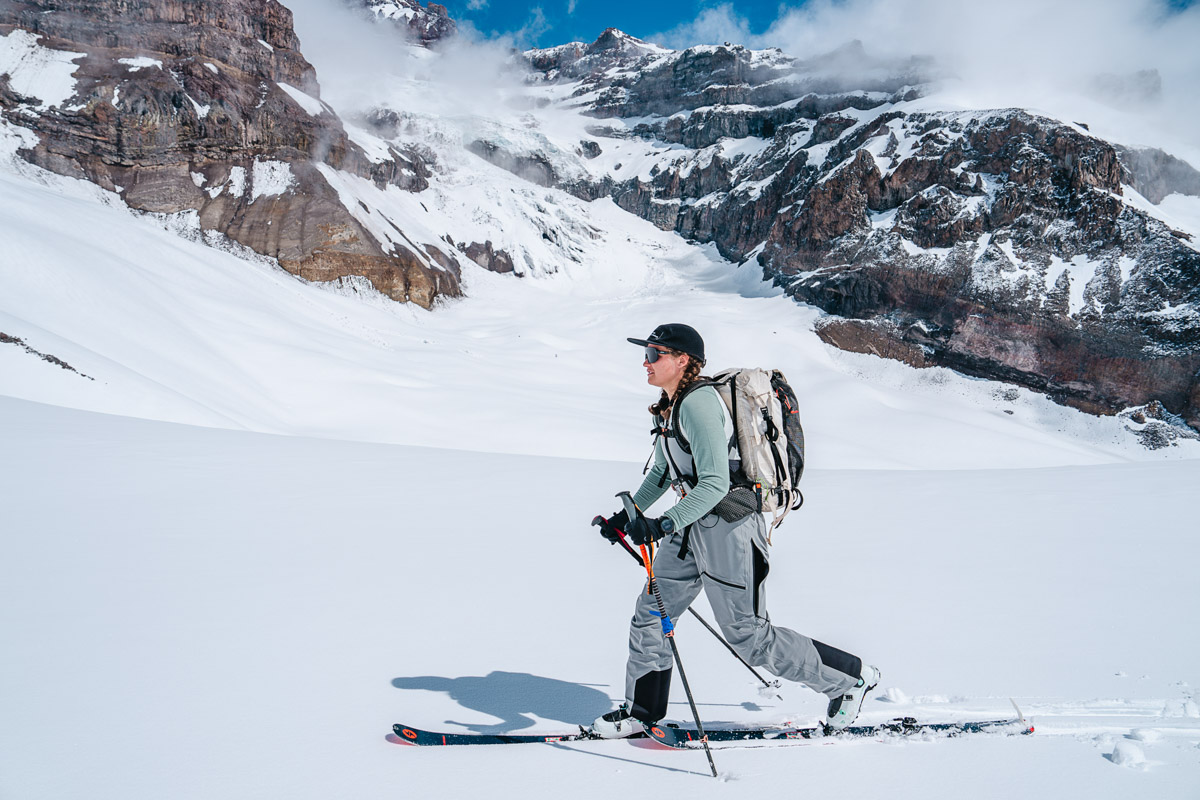 A woman skins across fresh snow with snowcapped mountains next to her