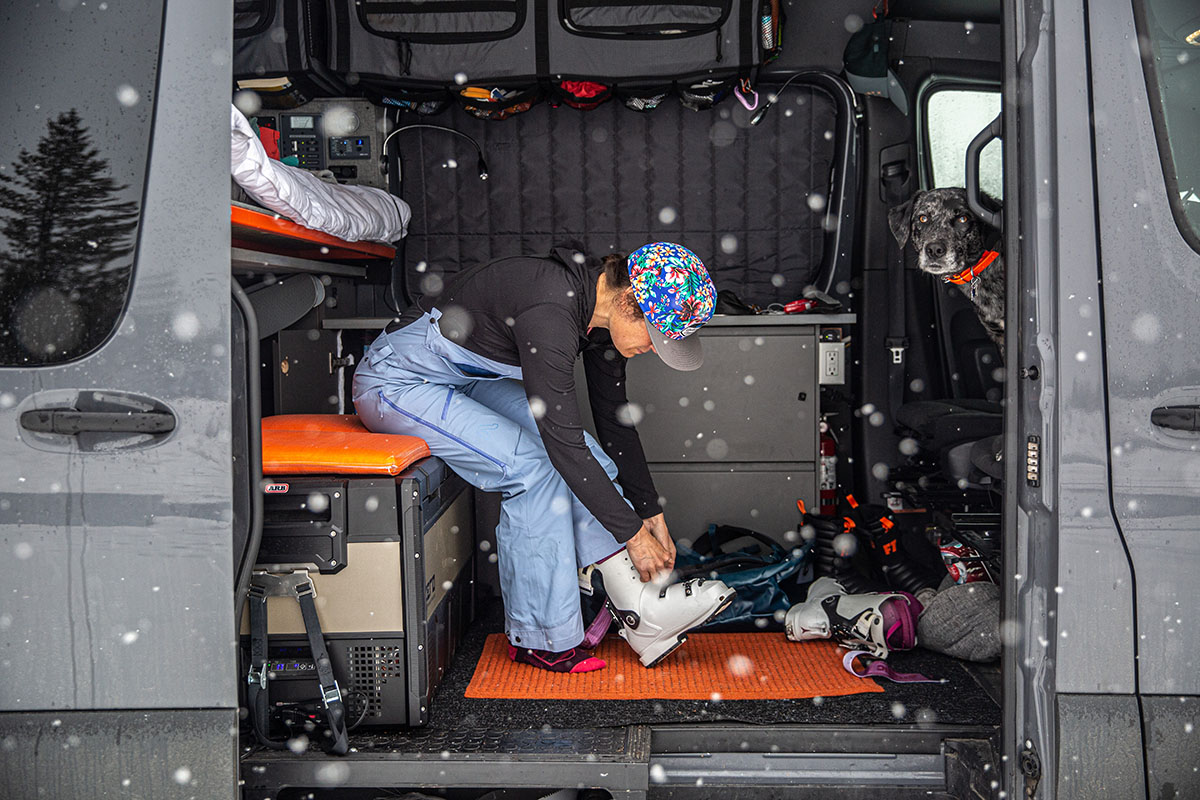 A woman inside a van puts on her ski boots