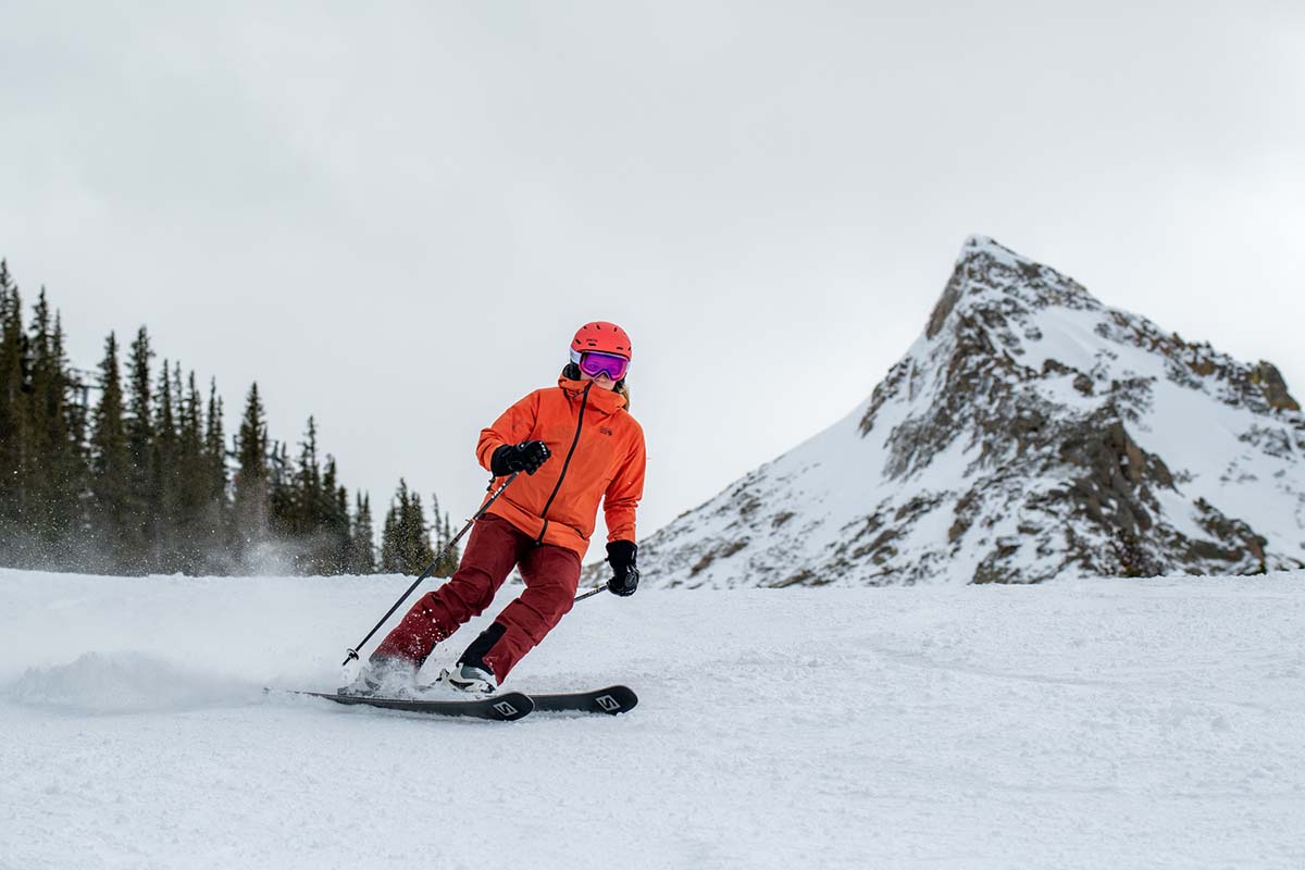 A woman in an orange jacket and red pants skis down a hill toward the camera