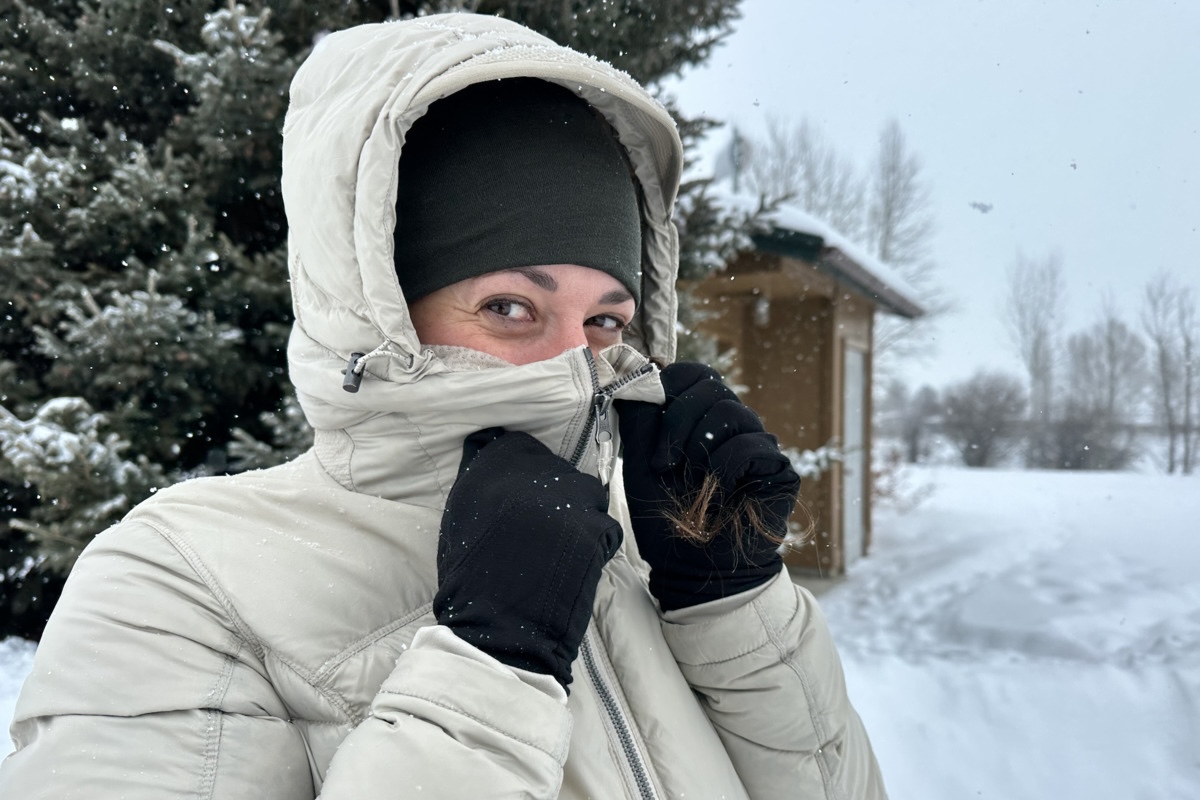 A woman pulls up the collar on a white winter jacket up over her nose
