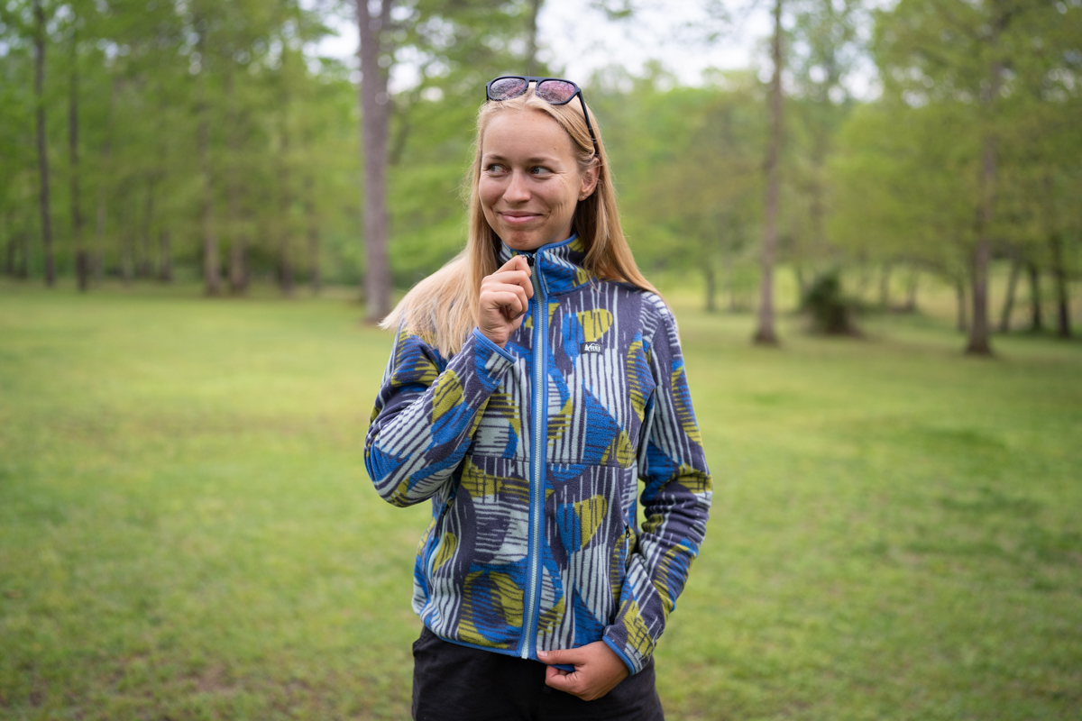 A woman zipping up a blue patterned fleece in a meadow
