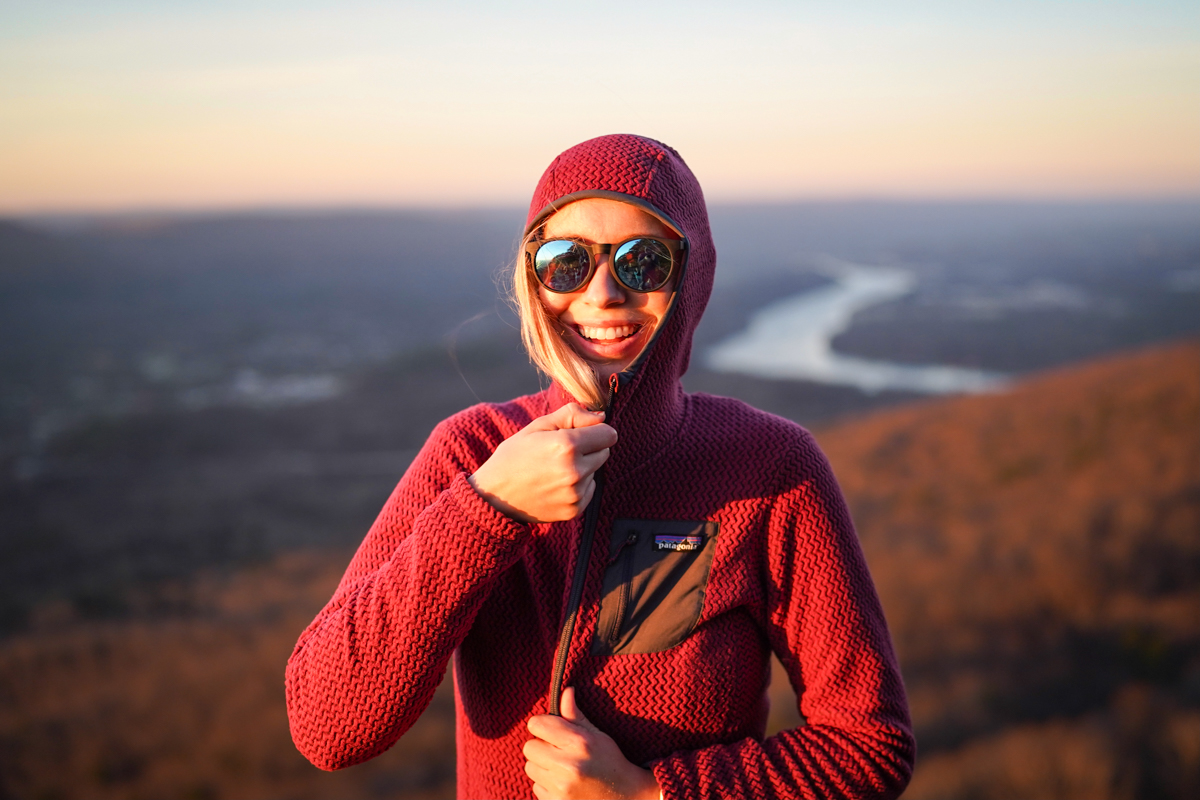 A woman zips up a grid fleece at an overlook