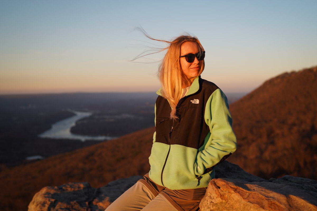 A woman stands on a windy overlook wearing a fleece jacket