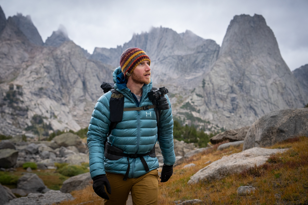 A man wearing a blue down jacket backpacks through mountainous environment