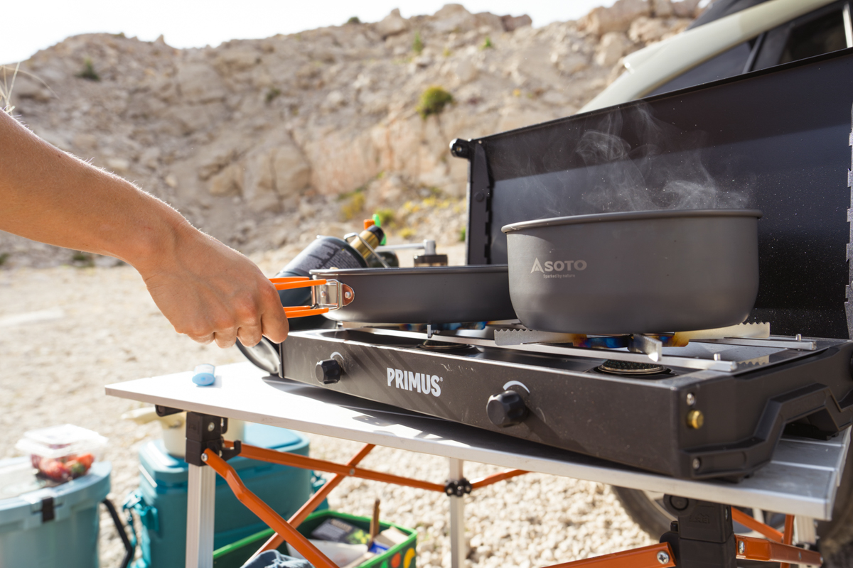 A hand adjusting a pot on a camping stove