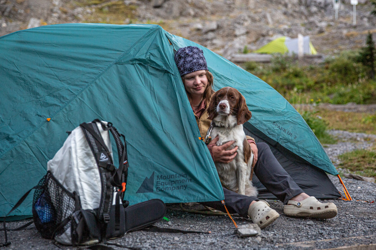 A woman sitting in a tent with a dog wearing camp shoes