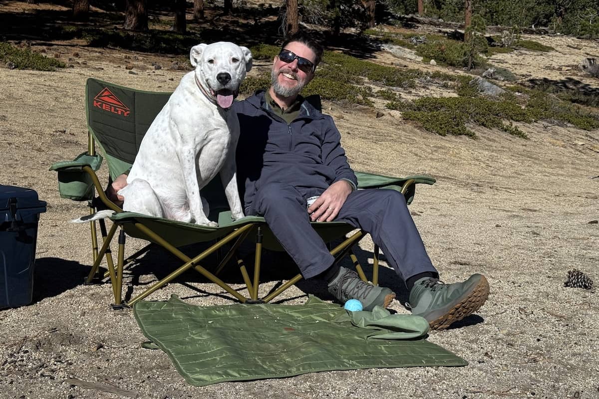A man and a dog sit side by side in a green two-person camping chair