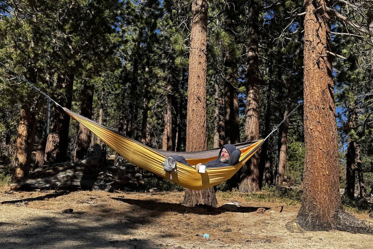 A man lounges in a yellow hammock with a cup of coffee