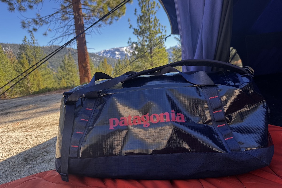 A blue duffel bag sits on the ground with mountains and trees in the background