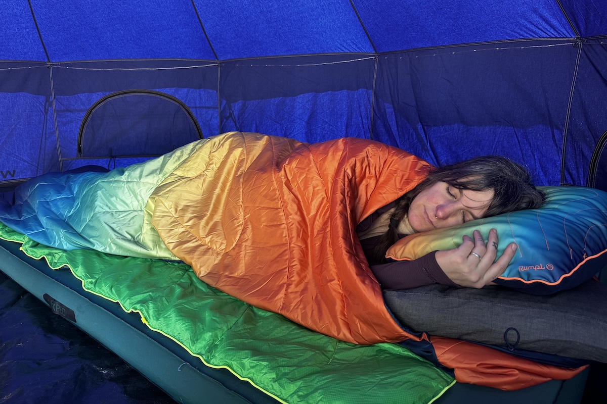 A woman sleeps under a colorful blanket in a blue tent