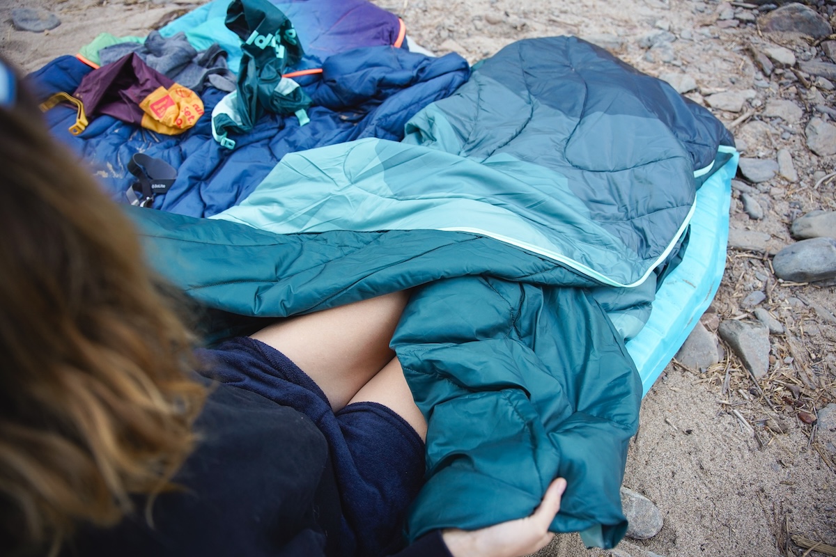 A woman is shown from the legs down unfolding the layers of the Rumpl Wrap Sack