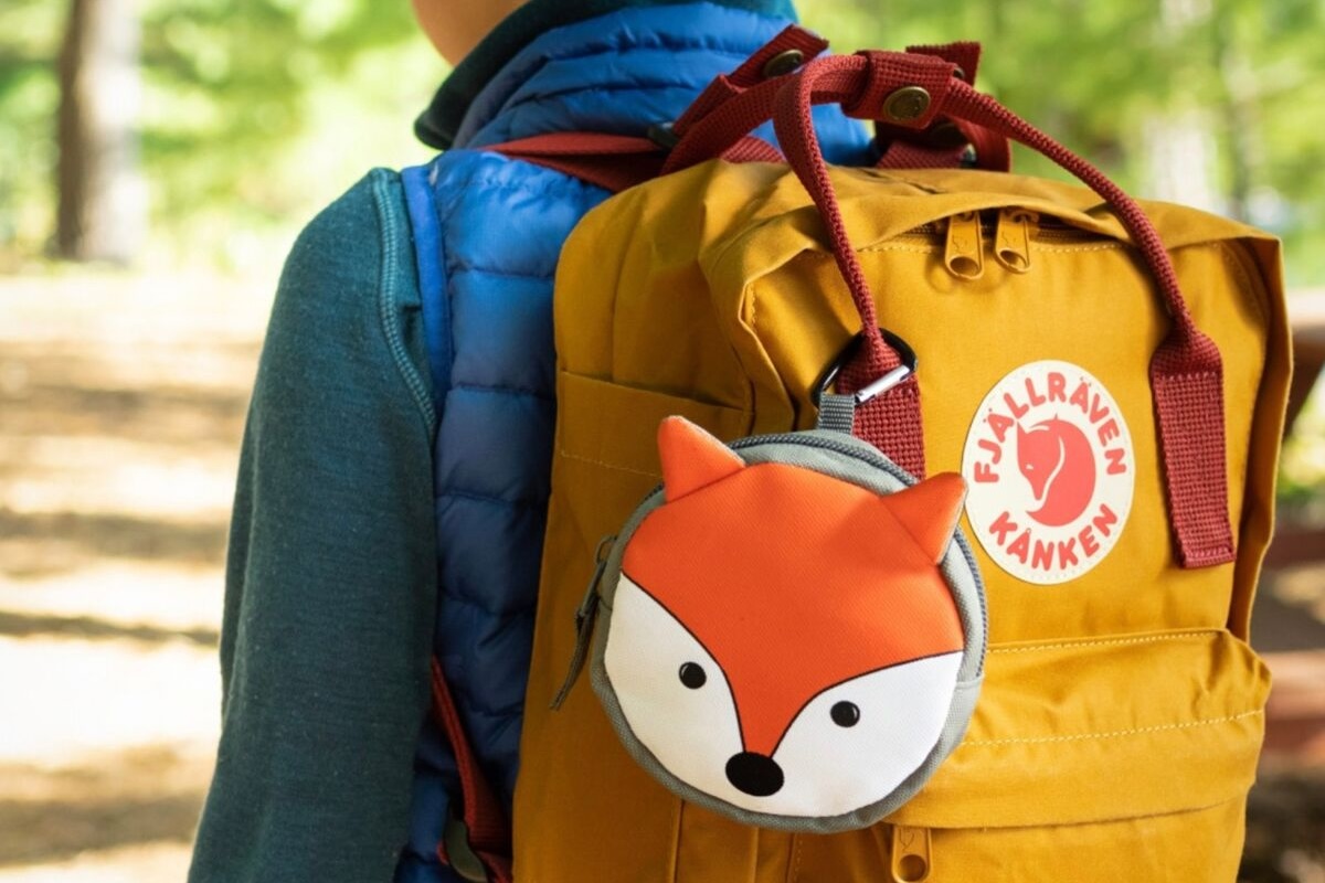 A first aid kit that looks like a fox is clipped to the side of a backpack