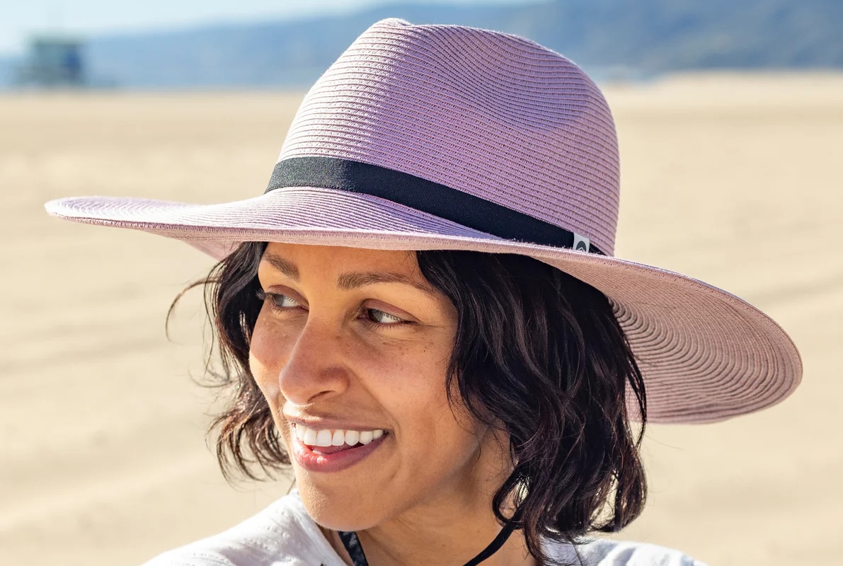 A woman smiles among the sand dunes while wearing a wide brimmed hat. 