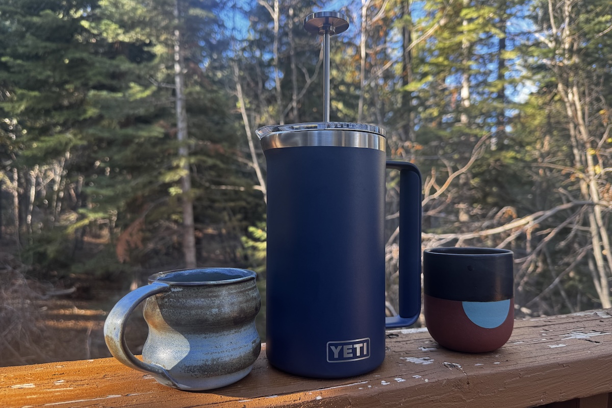 A blue French press with two handmade ceramic mugs sitting on a railing