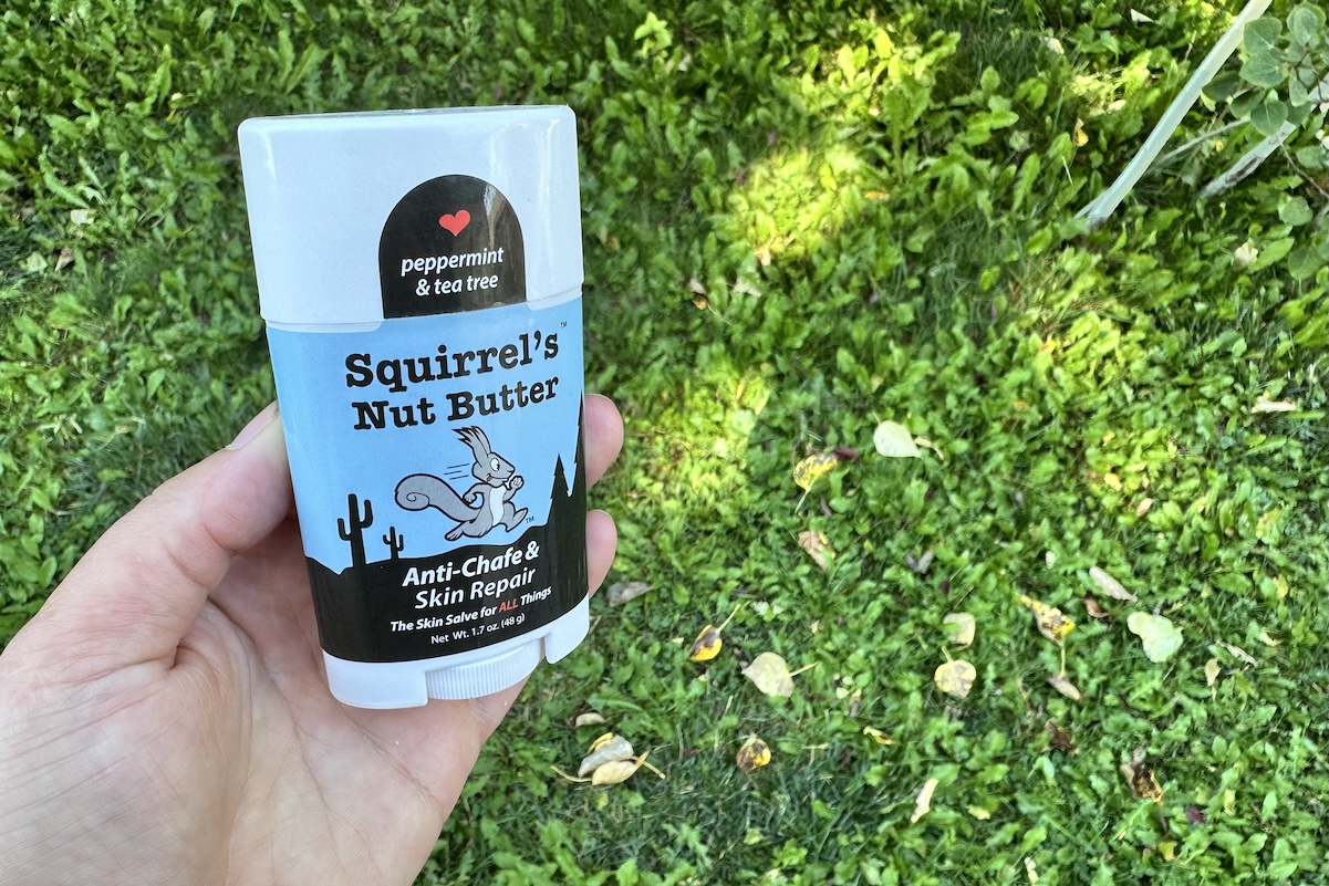 A hand holds squirrel's nut butter chafe cream over green grass