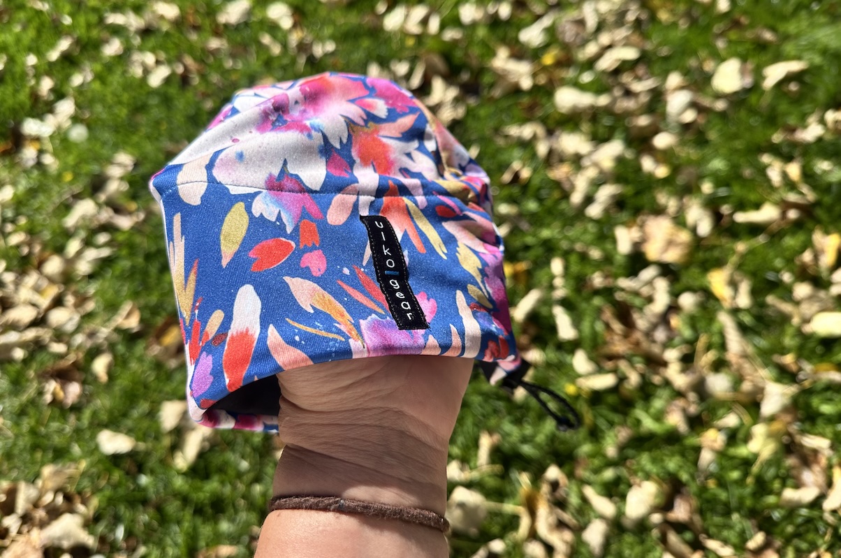 A hand holds a brightly colored winter running hat over a green lawn 