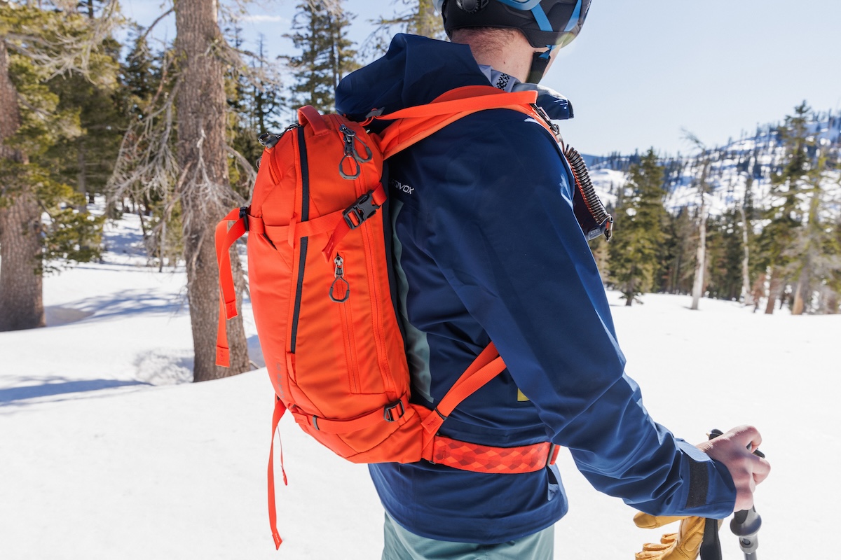 A closeup of an orange backpack on a suited-up skier
