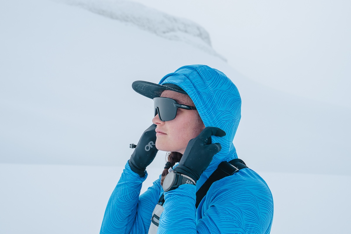 A woman wearing sunglasses pulls the hood of her baselayer up