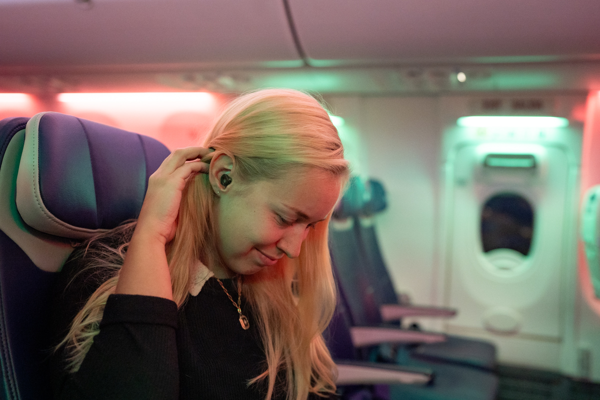 A woman uses earplugs on a plane to drown out background noise.