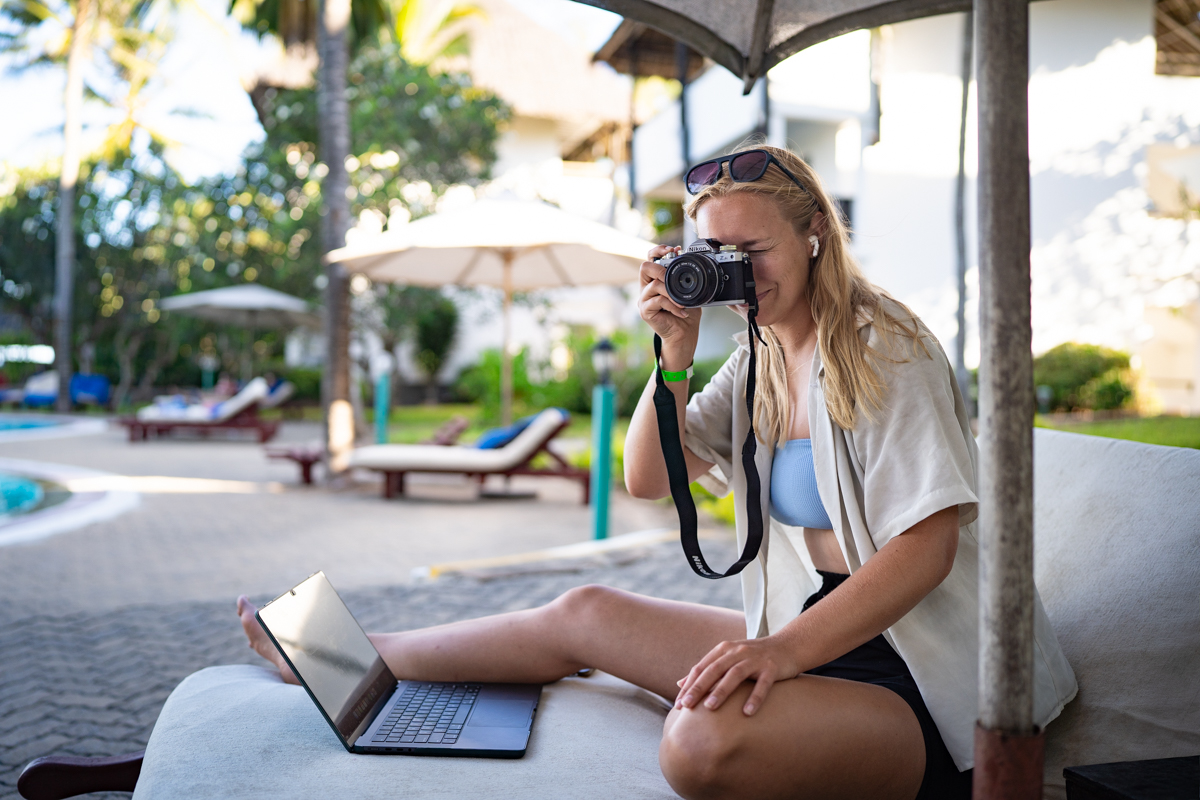 A woman enjoys lounging on a beach chair, while using her travel camera to take a shot.