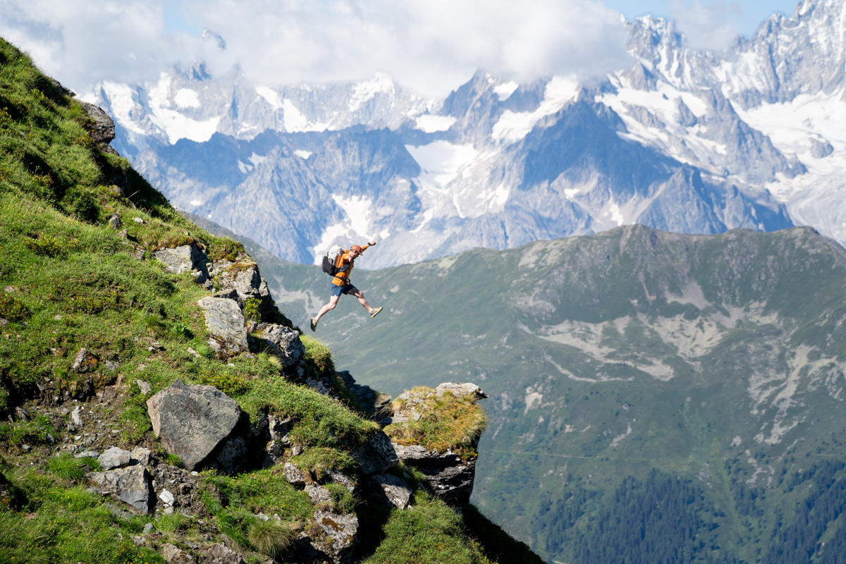 An adventurous hiker leaps from a mossy boulder with a stunning mountain vista in the background.